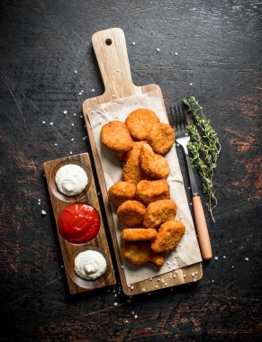 Kekik ve soslar ile bir kesme Tahtası üzerinde Tavuk nuggets. Koyu rustik arka plan üzerinde