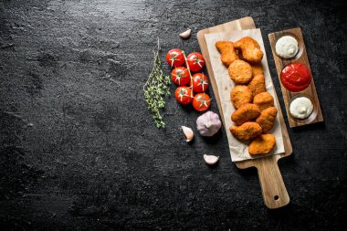 Farklı soslar, sarımsak ve domates ile bir kesme Kurulu tavuk nuggets. Siyah rustik arka plan üzerinde