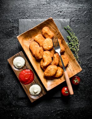 Çatal, kekik ve farklı soslar ile bir tabakta tavuk nuggets. Siyah rustik arka plan üzerinde