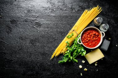 Makarna arka planı. Bolonya soslu kuru spagetti, otlar, domates ve peynir. Siyah rustik arka plan üzerinde