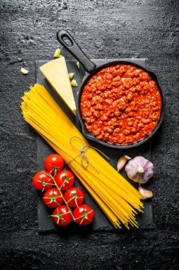 Makarna arka planı. Bolonya soslu kuru spagetti, domates ve sarımsak. Siyah rustik arka plan üzerinde
