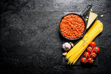 Makarna arka planı. Bolonya soslu kuru spagetti, domates ve sarımsak. Siyah rustik arka plan üzerinde