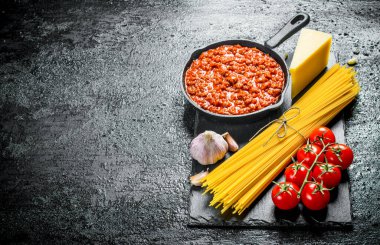Makarna arka planı. Bolonya soslu kuru spagetti, domates ve sarımsak. Siyah rustik arka plan üzerinde