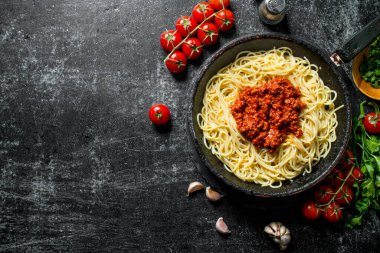 Domates, otlar ve sarımsak ile tavada Bolonya soslu Spagetti. Rustik arka planda