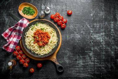 Domates, peçete ve kase doğranmış yeşillik ile tavada Bolonya soslu Makarna spagetti. Rustik arka planda