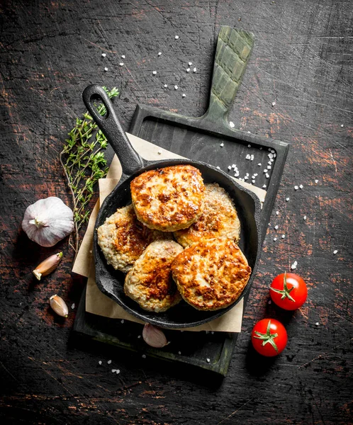 stock image Cutlets in pan on paper with thyme,garlic and tomatoes. On dark rustic background