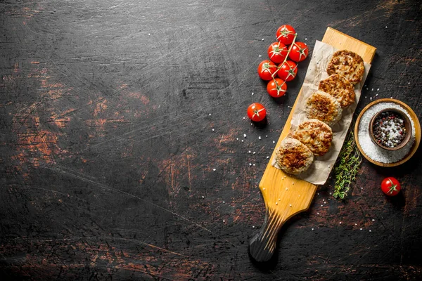 stock image Cutlets on paper with spices,thyme and tomatoes. On dark rustic background