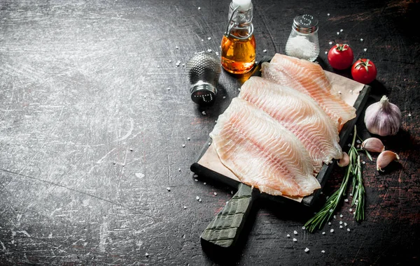 スパイス ローズマリー ニンニク 油を入れたまな板の上の魚の切り身 暗い素朴な背景に — ストック写真