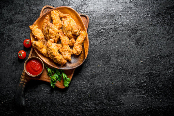 Chicken strips on a plate with parsley and sauce. On black rustic background