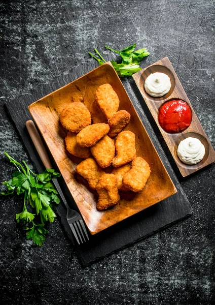 Yeşillik ve farklı soslar ile bir tabakta tavuk nuggets. Koyu rustik arka plan üzerinde