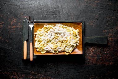 Bir bıçak ve çatal ile bir tabak üzerinde Carbonara soslu Fettuccine. Rustik arka planda