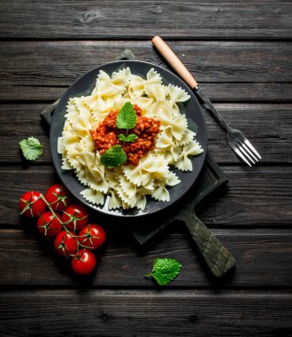 Domates ve nane yaprakları ile plaka üzerinde Bolonya soslu Makarna Farfalle. Siyah ahşap arka plan üzerinde