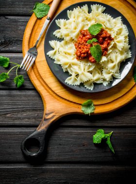 Bolonya soslu Farfalle makarna ve bir tabakta nane yaprakları. Siyah ahşap arka plan üzerinde