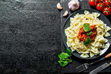 Bolonya soslu Farfalle makarna, domates, sarımsak ve nane yaprakları. Siyah rustik arka plan üzerinde