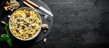 Mantar, sarımsak ve nane yaprakları ile tabakta fusilli yapıştırın. Siyah rustik arka plan üzerinde