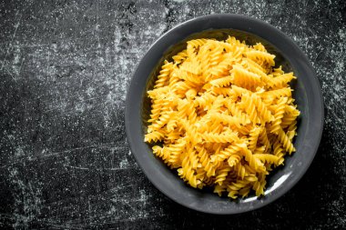 Kuru fusilli makarna bir kapta. Siyah rustik arka plan üzerinde