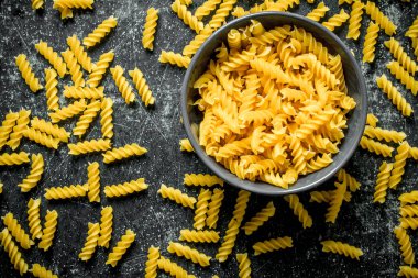Makarna arka planı. Siyah bir kapta kuru fusilli makarna. Siyah rustik arka plan üzerinde