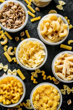 Makarna arka planı. Kaselerde farklı kuru makarna. Siyah rustik arka plan üzerinde