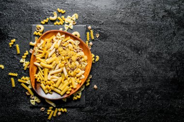 Makarna çeşitli bir tabakta kuru. Siyah rustik arka plan üzerinde