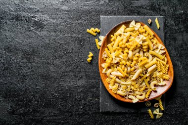 Makarna çeşitli bir tabakta kuru. Siyah rustik arka plan üzerinde