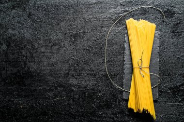Bir taş tahta üzerinde kuru makarna spagetti. Siyah rustik arka plan üzerinde