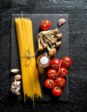 Domates, sarımsak, mantar ve yağ ile siyah taş Kurulu çiğ spagetti. Siyah rustik arka plan üzerinde