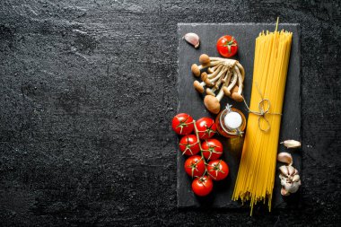 Domates, sarımsak, mantar ve yağ ile siyah taş Kurulu çiğ spagetti. Siyah rustik arka plan üzerinde