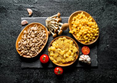 Domates, sarımsak ve mantar ile kaselerde çiğ hamur farklı. Siyah rustik arka plan üzerinde