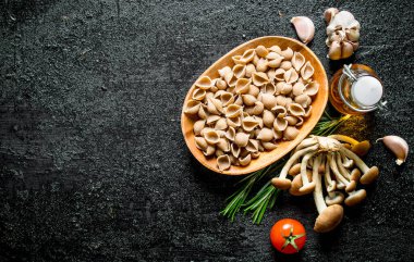 Yağ, mantar ve biberiye ile bir kapta Konkile çiğ hamur. Siyah rustik arka plan üzerinde