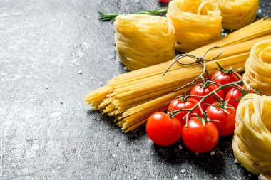 Domates ile spagetti ve tagliatelle çiğ. Siyah rustik arka plan üzerinde