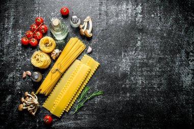 Spagetti, lazanya, tagliatelle yağ, domates ve mantar ile çiğ. Siyah rustik arka plan üzerinde