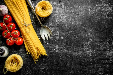 Çiğ spagetti ve tagliatelle kiraz domates, sarımsak ve bir kepçe ile. Siyah rustik arka plan üzerinde