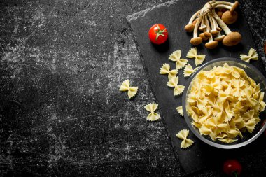 Mantar ve domates ile bir kapta Çiğ Farfalle makarna. Siyah rustik arka plan üzerinde