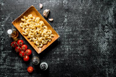 Domates, sarımsak ve baharat ile bir tabakta çiğ makarna. Siyah rustik arka plan üzerinde