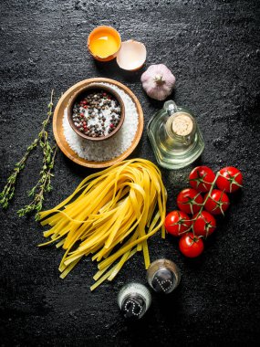 Baharat, yumurta, yağ ve domates ile çiğ ev pişmiş makarna. Siyah rustik arka plan üzerinde