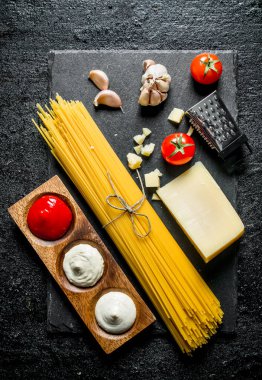 Parmesan ve farklı soslar ile ham spagetti. Siyah rustik arka plan üzerinde