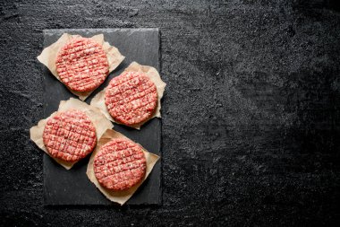 Kağıt üzerinde çiğ hamburger. Siyah rustik arka plan üzerinde