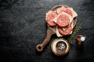 Baharat, yağ ve kekik ile kesme Kurulu çiğ burger. Siyah rustik arka plan üzerinde