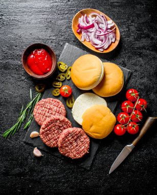 Domates, çörek, sos ve doğranmış soğan ile çiğ burger. Siyah rustik arka plan üzerinde