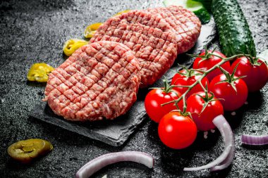 Soğan dilimleri, domates, biber ve salatalık ile çiğ burger. Siyah rustik arka plan üzerinde