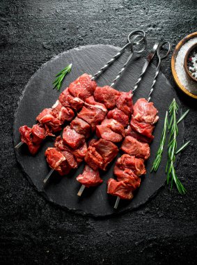 Biberiye ve baharatlar ile bir taş Tahta üzerinde çiğ sığır kebabı. Siyah rustik arka plan üzerinde