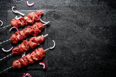 Soğan parçaları ile bir taş tahta üzerinde çiğ kebap. Siyah rustik arka plan üzerinde