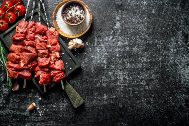 Raw kebab with tomatoes, spices and garlic cloves. On rustic background clipart