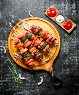 Soslar, biberiye ve soğan dilimleri ile bir kesme Kurulu üzerinde sebze ile çiğ sığır kebap. Rustik arka planda