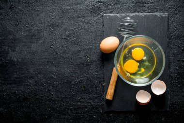 Çırpma teli ile kasede yumurta. Siyah rustik arka plan üzerinde