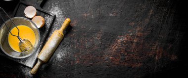 Çırpma teli ve oklava ile yumurta. Koyu rustik arka plan üzerinde