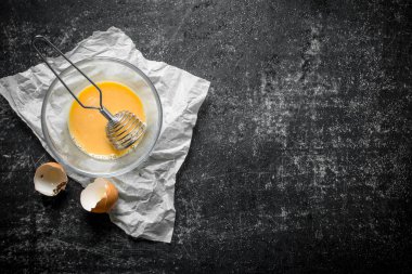 Bir kasede çırpılmış yumurta kağıda çırpılmış. Koyu rustik arka plan üzerinde