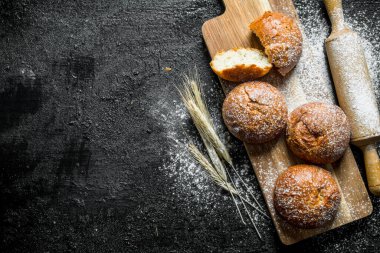 Bir oklava ve sivri ile ahşap kesme Tahtası üzerinde taze çörekler. Siyah rustik arka plan üzerinde