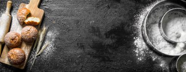 Bir elek un ile kokulu çörekler. Siyah rustik arka plan üzerinde