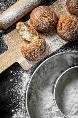 Bir elek un ile kokulu çörekler. Siyah rustik arka plan üzerinde
